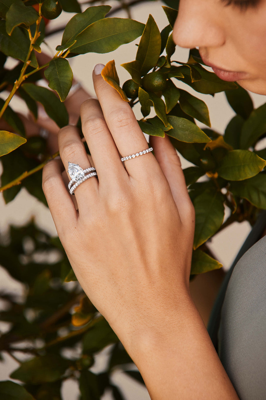 Close-up of a hand wearing two diamond rings with a blurred green leafy background